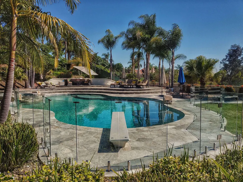 Glass pool fence around a freeform pool with a stone surround and palm trees