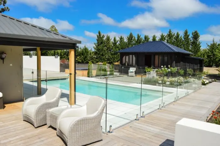 Glass pool fence between a timber deck with outdoor chairs and the pool